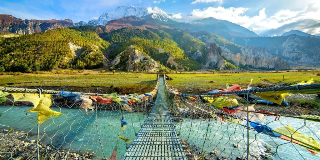 Prayer flags on a suspension bridge over a turquoise river, with the snow-capped Annapurna range behind